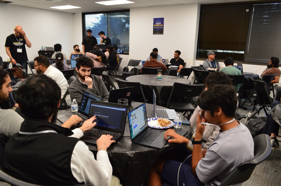 Teams heads-down at laptops around tables, building during the 48-hour sprint.